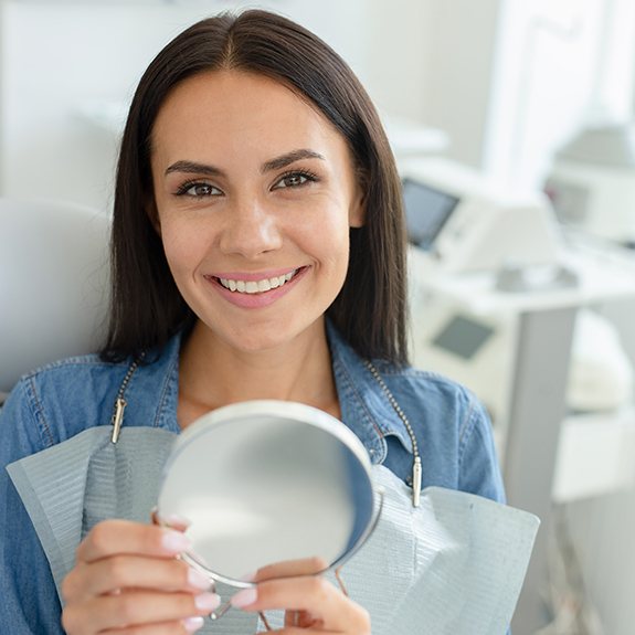 Happy dental patient holding hand mirror